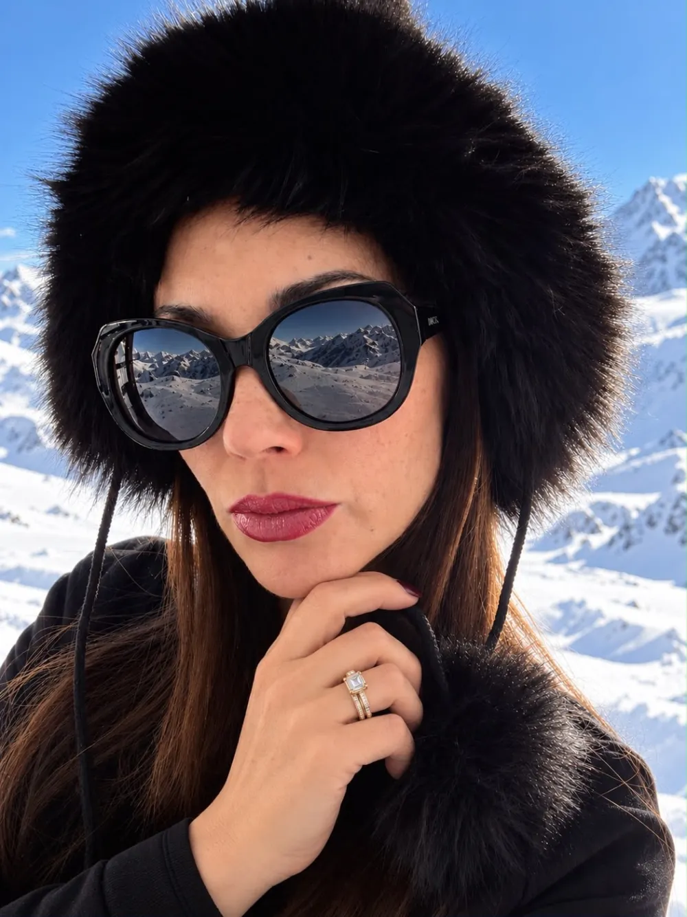Mujer con lentes de sol redondos y gorro de piel, con la montaña nevada reflejada en los cristales
